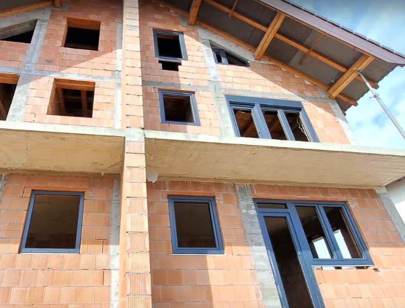 Ferestre și o ușă de balcon cu ramă antracit, montate pe o casă din cărămidă cu acoperișul în lucru
