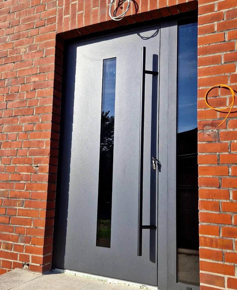 Anthracite entrance door with a vertical glass insert and a bar handle, in a brick wall