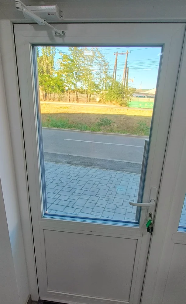 White glazed door with a handle, seen from inside, with a paved path in front of it