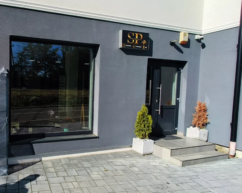Entrance with an anthracite door and a large shopfront window, on a grey facade, with the SP logo above the door