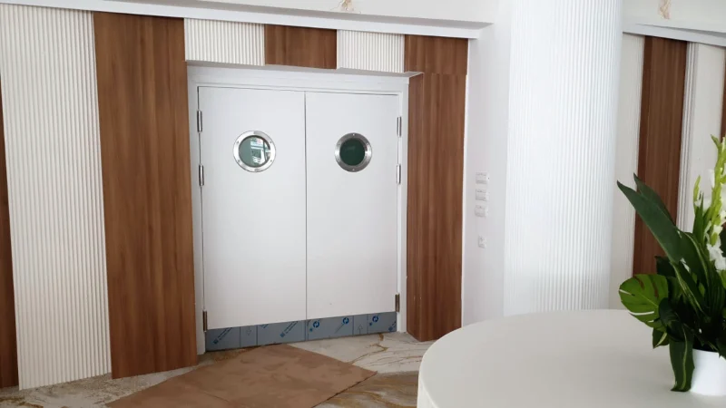 White double door with round windows, in a wall clad in wood and white fluting, during the works