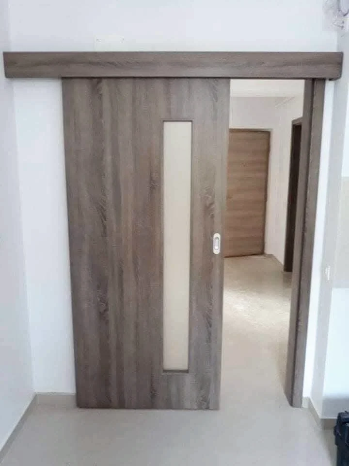 Sliding wood-effect door with a vertical glass insert, mounted on the wall