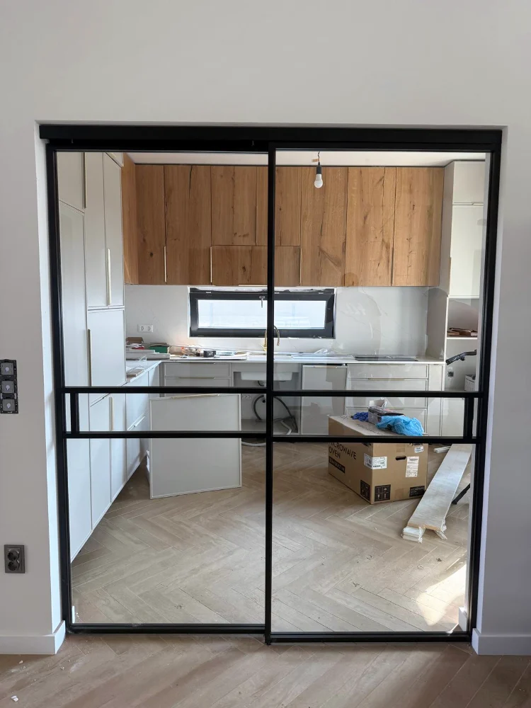 Partition with a black frame and glass between a room and the kitchen, with herringbone parquet