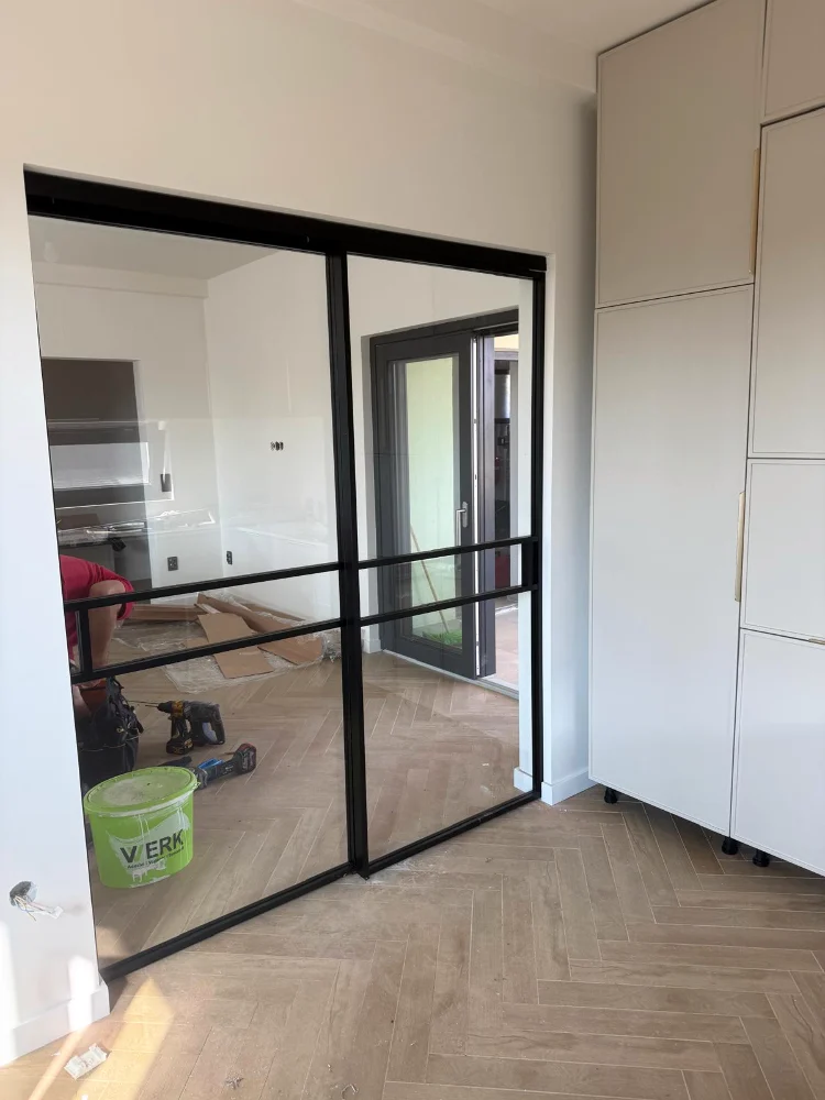 Partition with a black frame and glass in a room with herringbone parquet, during the works