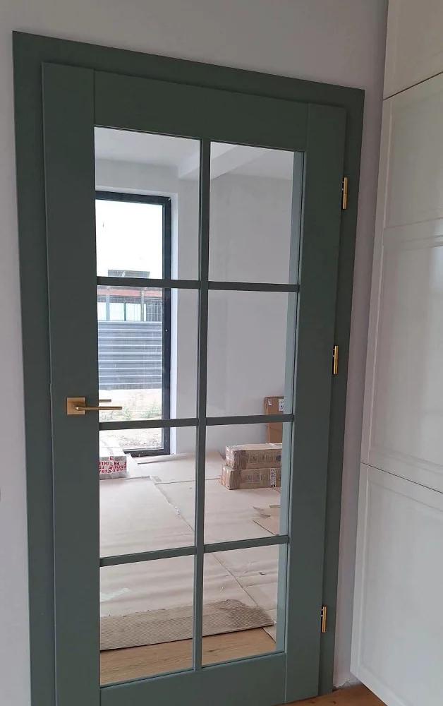 Green door with glass divided into eight squares, next to an oak parquet floor