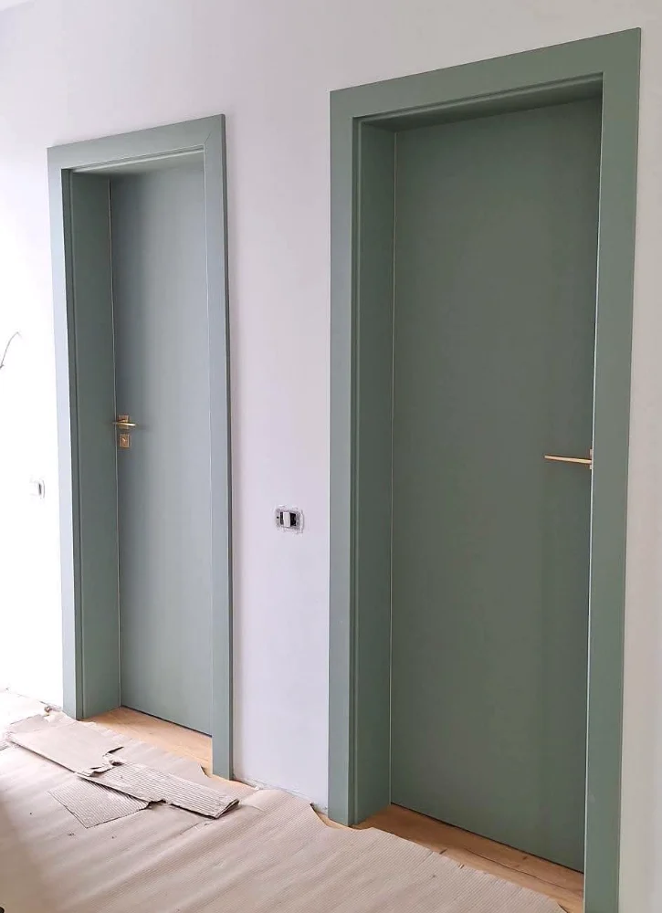 Two green-grey doors with frames in the same shade, in a white hallway, during the works